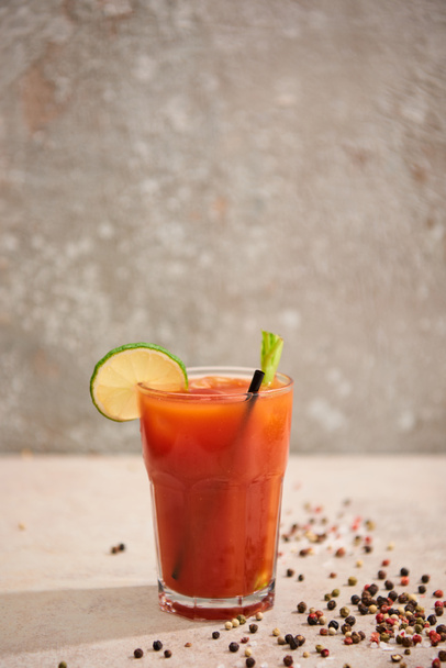 bloody mary cocktail in glass with lime, celery and straw on grey background with black pepper - Photo, Image