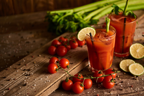 bloody mary cocktail in glasses on wooden background with salt, pepper, lime, tomatoes and celery - Photo, Image