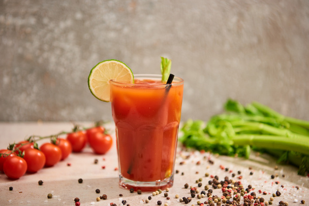 selective focus of bloody mary cocktail in glass with straw and lime near salt, pepper, tomatoes and celery on grey background - Photo, Image