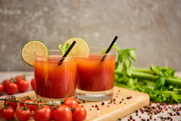 bloody mary cocktail in glasses with straws and lime on wooden board near salt, pepper, tomatoes and celery - Photo, Image