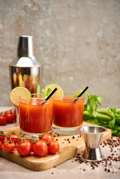 blutiger Marzipan-Cocktail in Gläsern mit Strohhalmen und Limetten auf Holzbrettern in der Nähe von Salz, Pfeffer, Tomaten und Sellerie - Foto, Bild