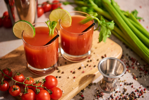 bloody mary cocktail in glasses on wooden board near salt, pepper, lime slices, tomatoes and celery - Photo, Image