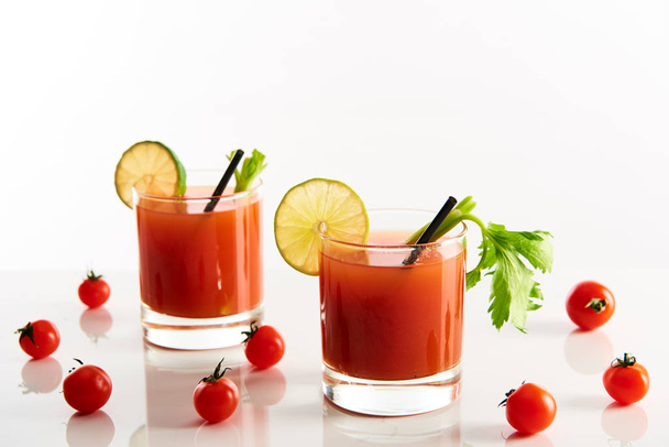 bloody mary cocktail in glasses garnished with lime and celery isolated on white with tomatoes - Photo, Image