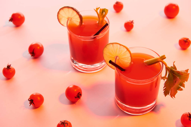 blutiger Mary-Cocktail in Gläsern garniert mit Limette und Sellerie auf rot beleuchtetem Hintergrund mit Tomaten - Foto, Bild