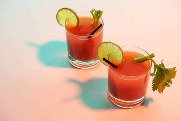 bloody mary cocktail in glasses garnished with lime and celery on red and blue illuminated background - Photo, Image