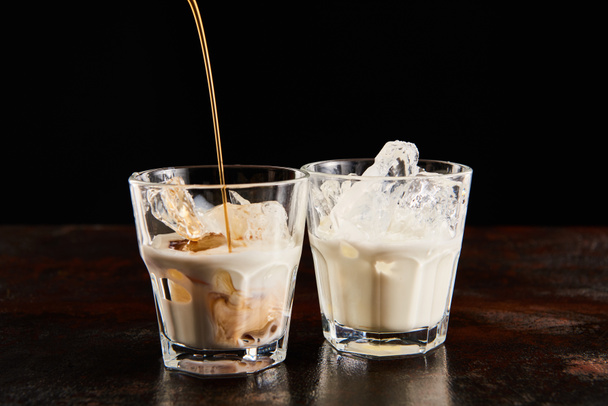 coffee liquor poring in glasses with ice cubes isolated on black - Fotó, kép