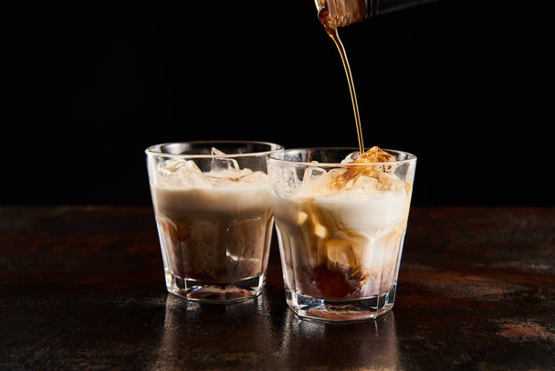 coffee liquor poring in glasses with ice cubes isolated on black - Fotó, kép