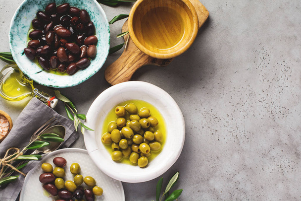 Several varieties of fresh olives in different ceramic plates on an old vintage gray table concrete background. Natural product concept. Rustic vintage set of cutlery. Top view, copy space. - Foto, Imagem