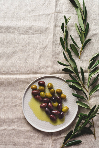 Several varieties of fresh olives in different ceramic plates on an old vintage gray napkin tablecloth table background. Natural product concept. Rustic vintage set of cutlery. Top view, copy space. - Фото, изображение