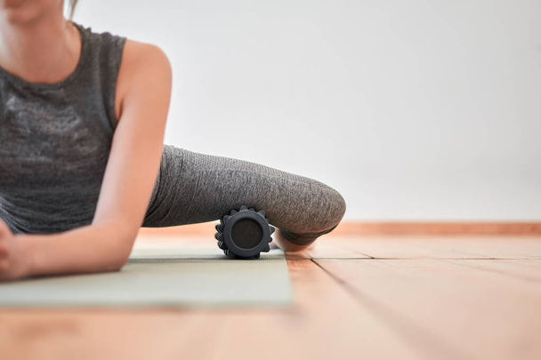Woman stretching with massager sitting on rug - 写真・画像