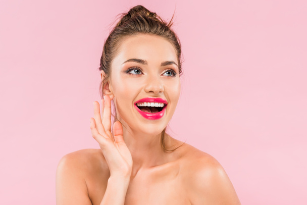 happy naked beautiful woman with pink lips posing with hand near face isolated on pink  - Фото, зображення