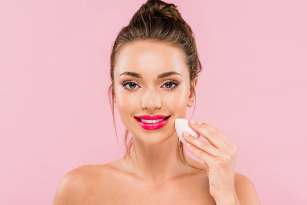 smiling naked beautiful woman with pink lips holding makeup sponge isolated on pink  - Foto, afbeelding