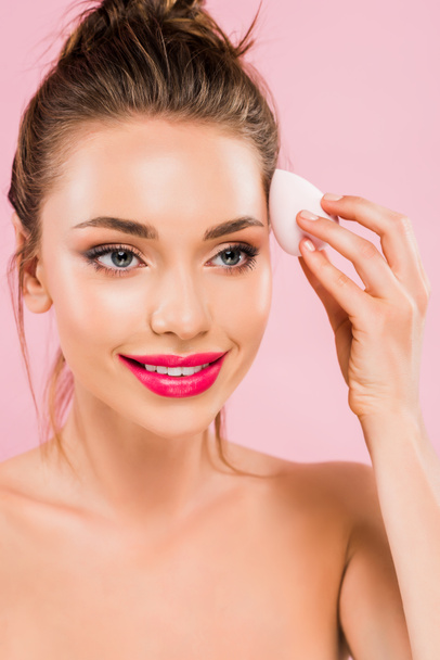 smiling naked beautiful woman with pink lips holding makeup sponge isolated on pink  - Foto, Imagen