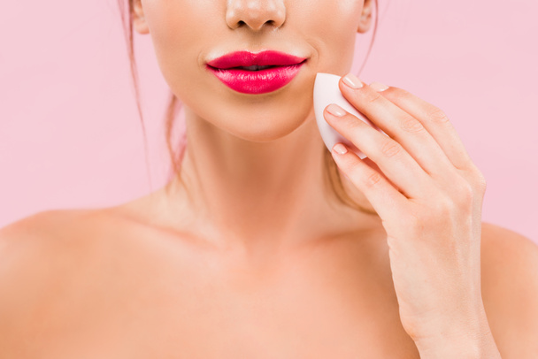 cropped view of naked beautiful woman with pink lips holding makeup sponge isolated on pink  - Фото, изображение