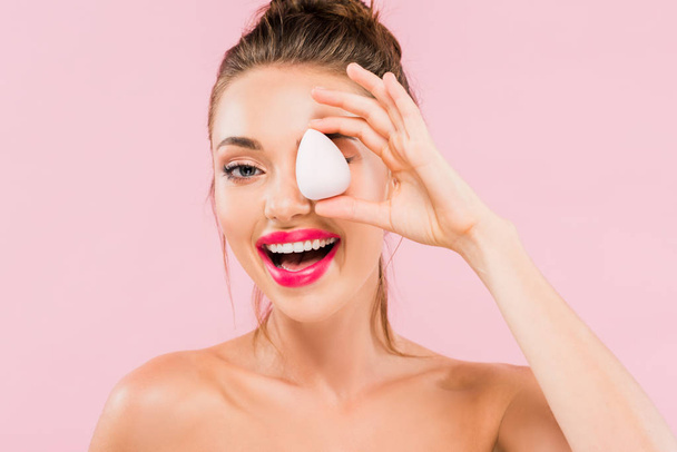 happy naked beautiful woman with pink lips and open mouth holding makeup sponge isolated on pink  - Photo, image
