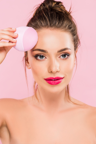 naked beautiful woman with pink lips holding facial cleansing brush isolated on pink  - Fotoğraf, Görsel