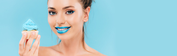 mosolygós meztelen gyönyörű nő kék ajkak és cupcake elszigetelt kék, panorámás lövés - Fotó, kép