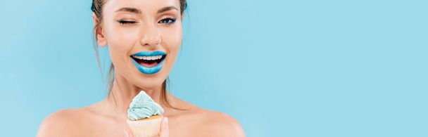 sorrindo mulher bonita nua com lábios azuis e cupcake piscar isolado em azul, tiro panorâmico
 - Foto, Imagem