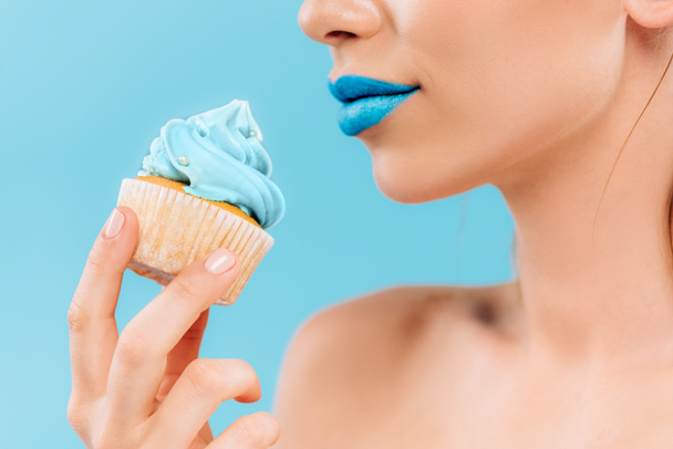 partial view of naked beautiful woman with blue lips holding cupcake isolated on blue - Foto, Imagem