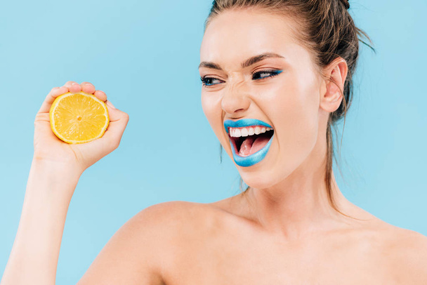 angry naked beautiful woman with blue lips holding orange half isolated on blue - Foto, Imagen