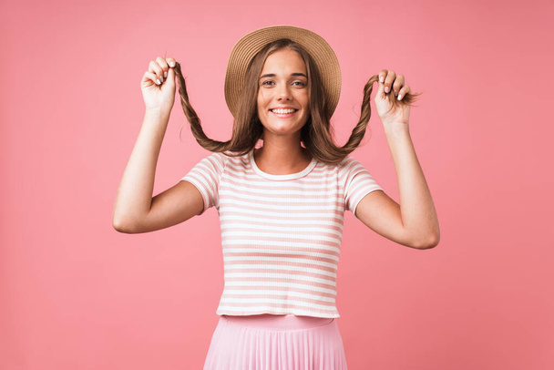 Image of young happy woman wearing straw hat making fun with her hair while smiling at camera - Foto, afbeelding