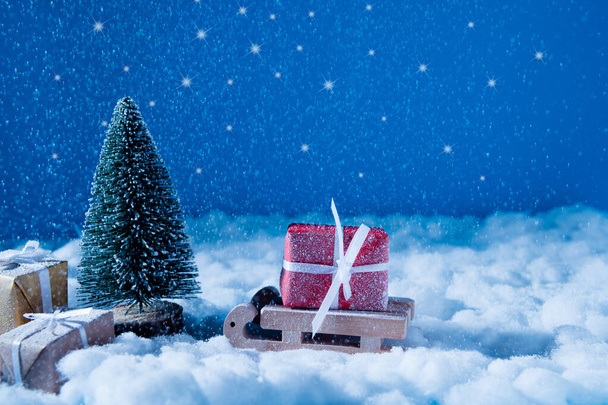 İzlanda 'daki Noel Baba yer atölyesine gelen küçük tahta kızak resmi. Büyük kırmızı hediye kutusu, yeni yıl karlı akşam mucizesi, sihirli gece konsepti. - Fotoğraf, Görsel