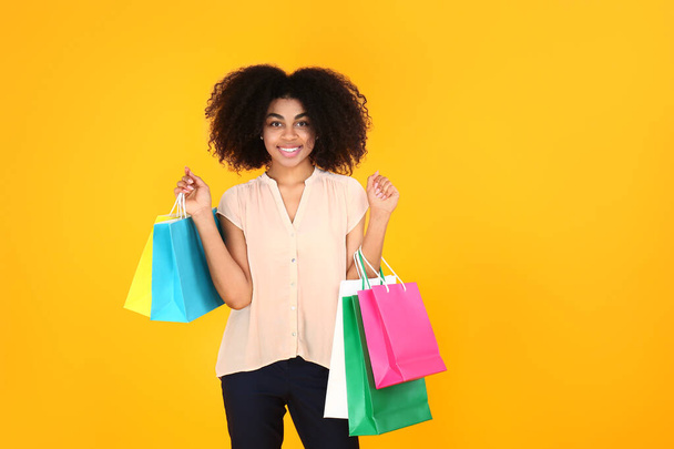 Beautiful African-American woman with shopping bags on color background - Photo, Image