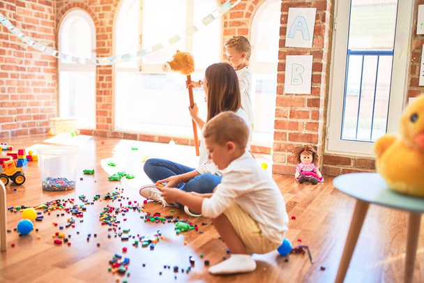 Όμορφη δασκάλα και νήπια παίζουν γύρω από πολλά παιχνίδια στο νηπιαγωγείο - Φωτογραφία, εικόνα