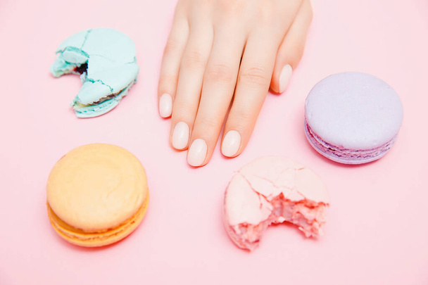 Stylowy modny manicure kobiet na różowym tle. Dziewczyna ręce makaron ciasteczka - Zdjęcie, obraz