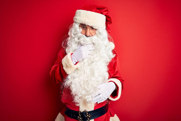 Keski-ikä komea mies yllään Santa puku seisoo yli eristetty punainen tausta Näyttää kiehtonut epäusko, yllätys ja hämmästynyt ilme kädet leualla
 - Valokuva, kuva