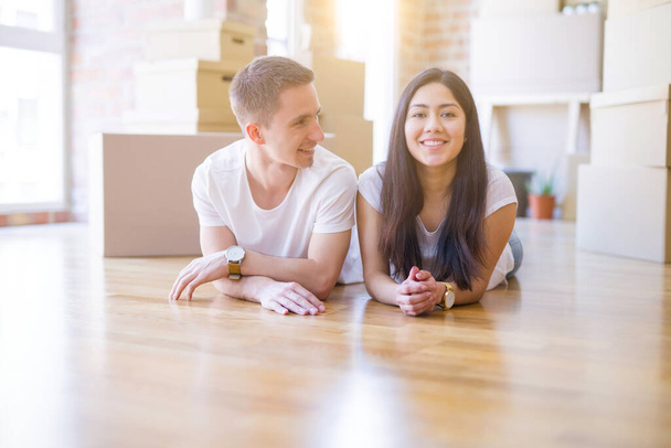 Young beautiful couple lying down at new home around cardboard boxes - Photo, Image