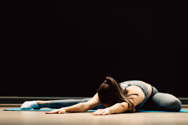 Athletic girl stretching lying on rug in sports hall - Фото, зображення