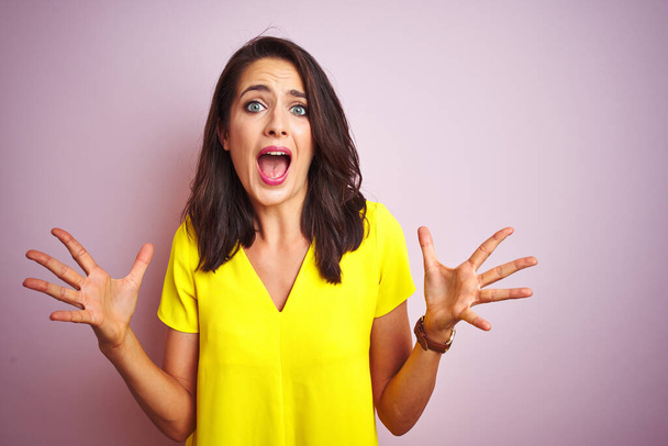 Young beautiful woman wearing yellow t-shirt standing over pink isolated background celebrating crazy and amazed for success with arms raised and open eyes screaming excited. Winner concept - Foto, Imagen