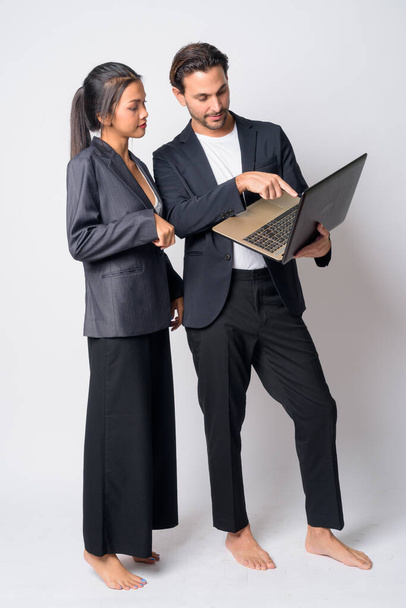 Full body shot of multi ethnic business couple using laptop together - 写真・画像