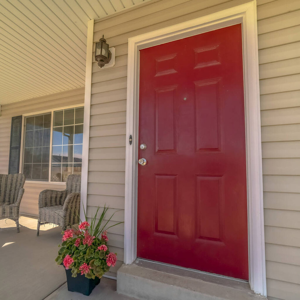 Kwadratowa rama Błyszczący czerwony drewniane drzwi frontowe domu z wiklinowymi krzesłami na słonecznym ganku - Zdjęcie, obraz
