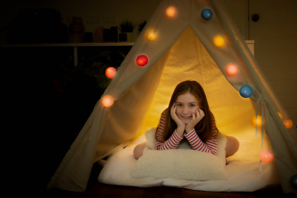 Mutlu küçük kız gülümsüyor ve evdeki çadırlarda kamp yapıyor. - Fotoğraf, Görsel