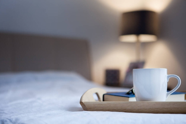 Cup of hot drink and book on bed - Valokuva, kuva