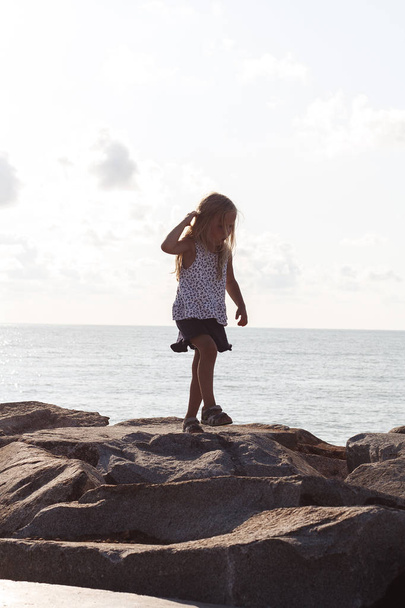 Little girl walks on the stones along the seashore - 写真・画像