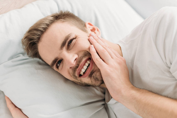 молодий чоловік лежить у ліжку і страждає від зубного болю
 - Фото, зображення