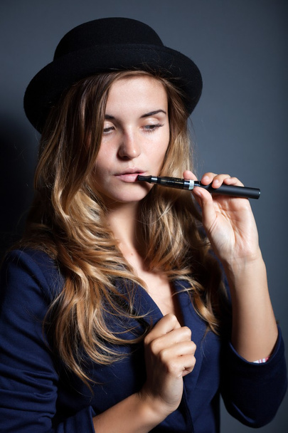Elegant woman smoking e-cigarette wearing suit and hat - Valokuva, kuva