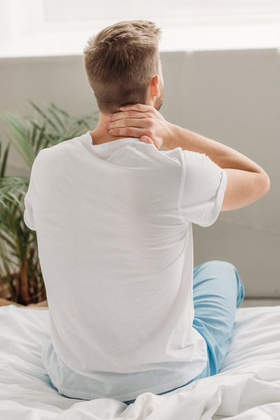 back view of man sitting on white bedding and suffering from neck pain - Photo, Image