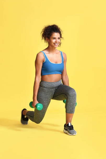 Sporty African-American woman with dumbbells on color background - Фото, изображение