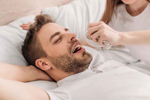 cropped view of woman holding hanky near face of snoring husband - Photo, Image