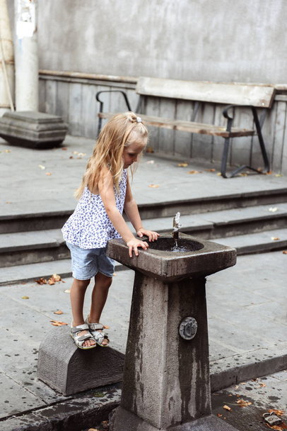 young beautiful girl playing outdoors with the fountain  - Fotografie, Obrázek