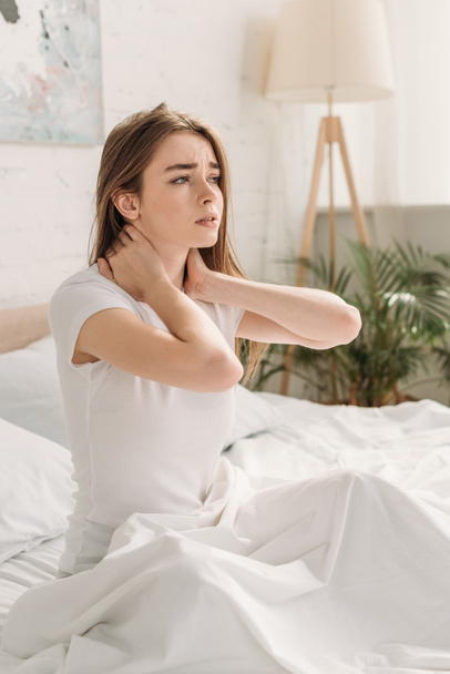 upset girl looking away while sitting in bed and suffering from neck pain - Foto, Bild