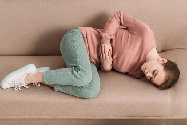 お腹の痛みを抱えながらソファに寝そべっている不幸な女性 - 写真・画像
