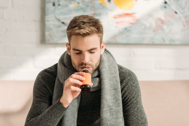 άρρωστος άνθρωπος σε ζεστό κασκόλ πίνοντας σιρόπι βήχα με κλειστά μάτια - Φωτογραφία, εικόνα
