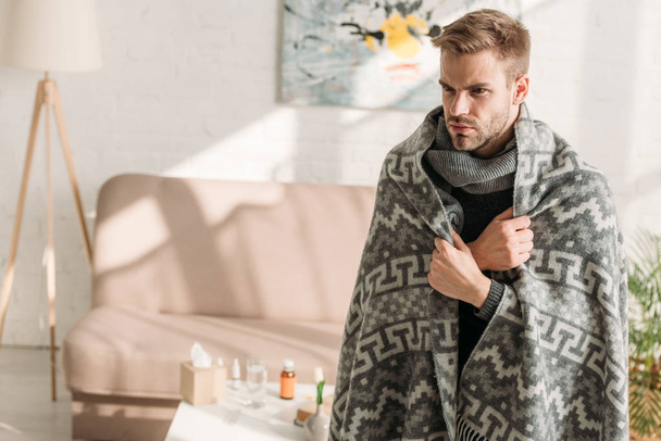 sick, unhappy man, wrapped in blanket, looking away while standing in room - Photo, Image