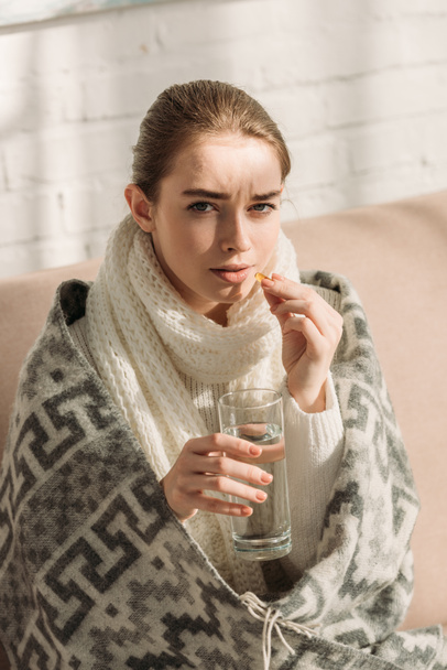 sick girl looking at camera while holding glass of water and taking medicine - Foto, Imagem