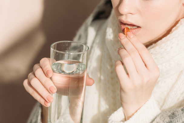 обрезанный вид больной женщины, держащей стакан воды во время приема лекарств
 - Фото, изображение